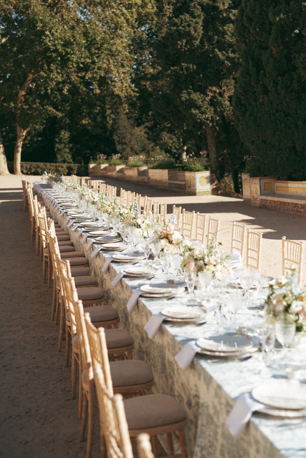 Long wedding table with toile linens stretching under tall trees