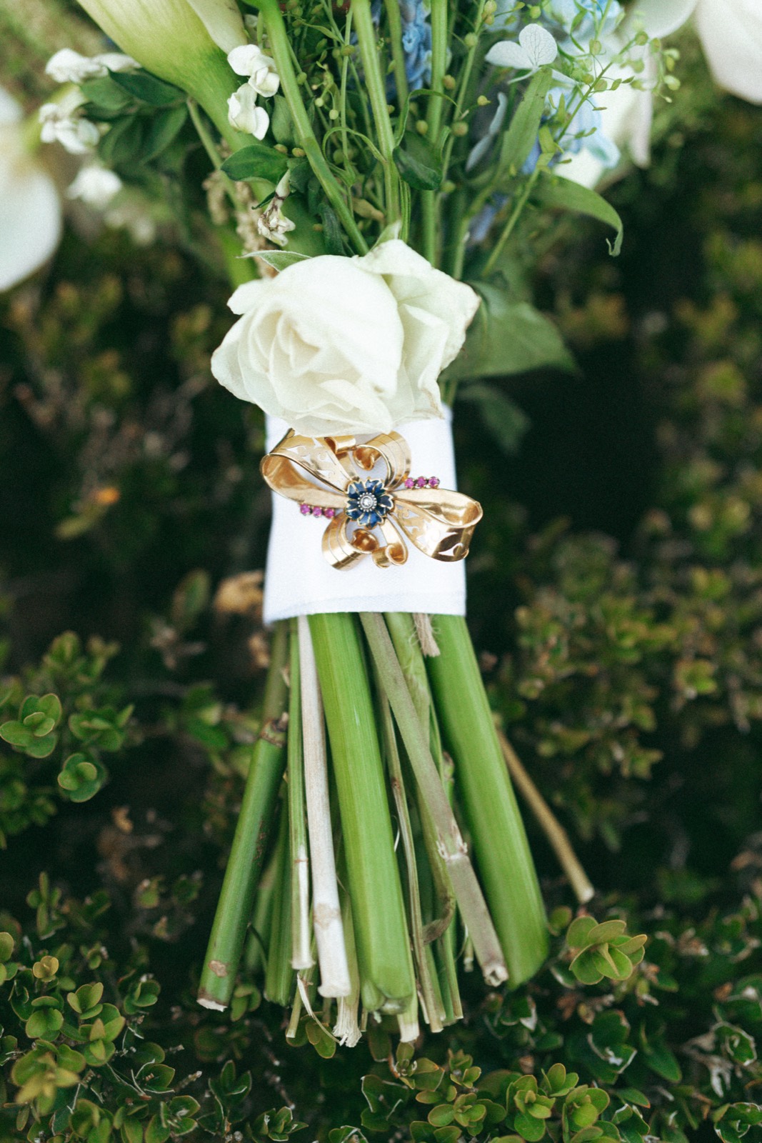 Bridal bouquet wrapped with a gold brooch, resting among greenery