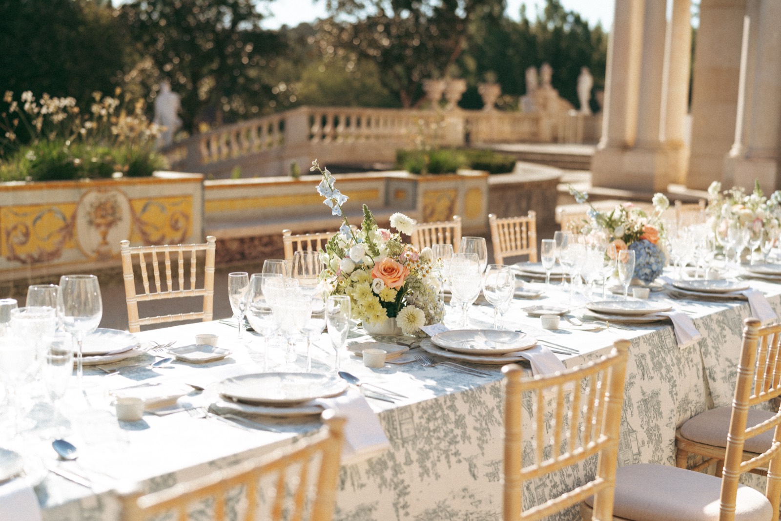 Place settings with glassware, florals and blue toile linens beside a tiled garden wall