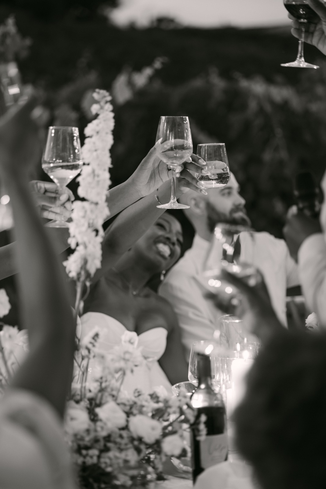 Black and white photo of guests raising glasses in a toast, with the bride laughing in the center